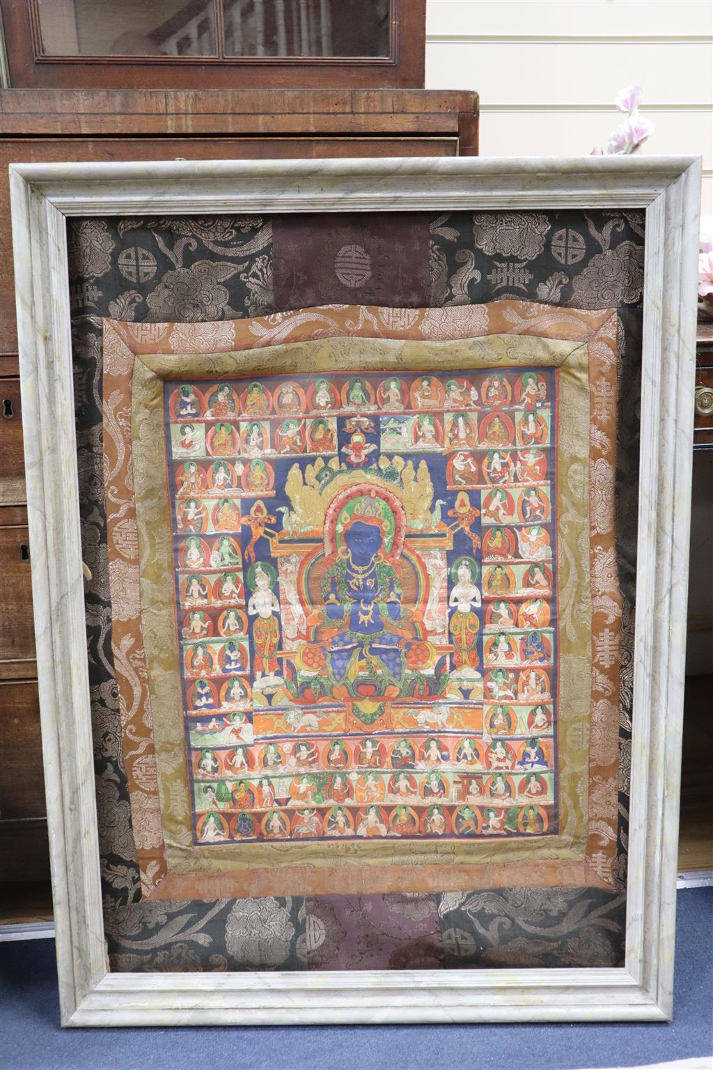 A Tibetan painted silk thangka with a blue Buddha surrounded by figures, central panel 54 x 43cm, overall 86 x 60cm